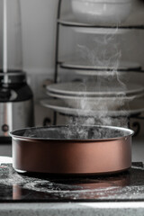 Boiling water with steam in a brown stewing pan on an electric stove in the kitchen. 