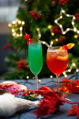 Vibrant green and red festive cocktails garnished with cherries and citrus slices, set against a backdrop of holiday lights and Christmas decorations.