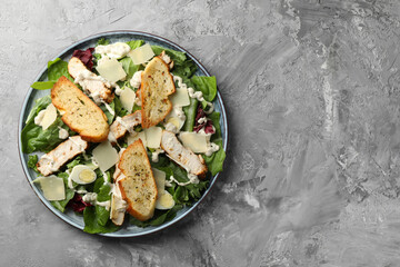 Tasty Caesar salad with chicken on gray textured table, top view. Space for text