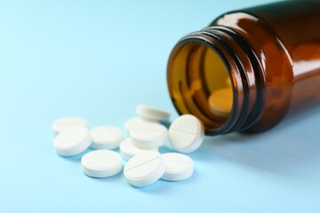 Bottle of antibiotic pills on light blue background, closeup