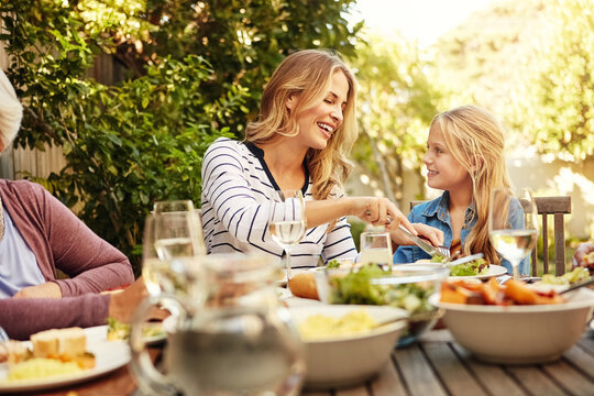 Family, mom and child at outdoor lunch with smile, celebration and eating together in backyard. Care, mother and daughter at table for garden picnic with food, drinks and happy bonding on patio. - Powered by Adobe