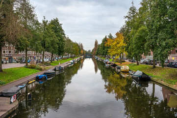 Obraz premium The Erasmusgracht or canal with small vessels and trees reflecting in the water in Amsterdam, The Netherlands