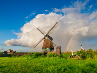 Fototapeta premium Landscape with windmill and rainbow. Dutch. A huge cloud after a storm. Agricultural fields and pastures. Summer landscape in the Netherlands. Photo for background, wallpaper, postcards.