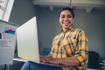 Photo of lovely young lady working hold netbook dressed yellow plaid shirt comfortable startup office loft room interior