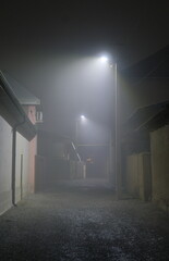 A foggy street at night with bright streetlights illuminating the road. 