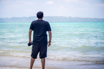 Young man standing on havelock beach staring out over the blue turquoise waters of andaman sea