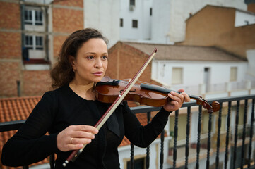 Woman playing violin on a balcony overlooking city buildings