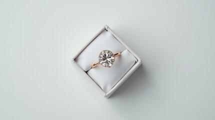  A white box with a diamond ring inside. The ring is in a diamond shape and is placed in the center...