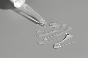 Dripping cosmetic serum from pipette on grey background, closeup