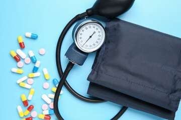 Blood pressure measuring device and pills on light blue background, top view