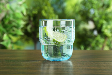 Glass of soda water with lime on wooden table against blurred background