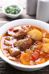 Delicious stew with vegetables in bowl on wooden table, closeup
