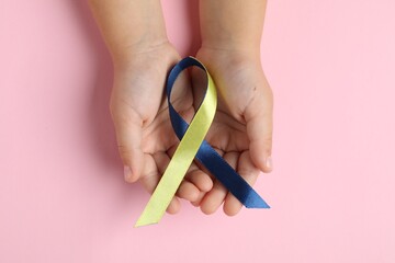 Child with yellow and blue ribbon on pink background, top view. Down syndrome awareness