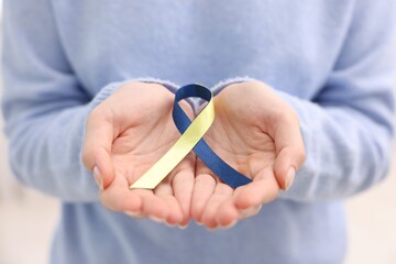 Woman with yellow and blue ribbon on light background, closeup. Down syndrome awareness