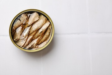 Tasty sprats in tin can on white tiled table, top view. Space for text