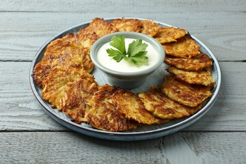 Delicious potato pancakes and sour cream on gray wooden table, closeup