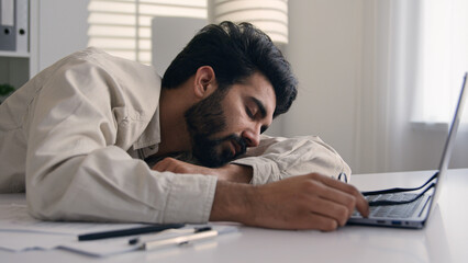 Obraz premium Lazy weary sleepy male manager tired exhausted Arabian Indian businessman employee working computer boring remote job man fall sleep on desktop napping in office overwork fatigue no energy sleeping