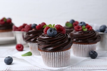 Tasty cupcakes with chocolate cream and berries on white wooden table, closeup