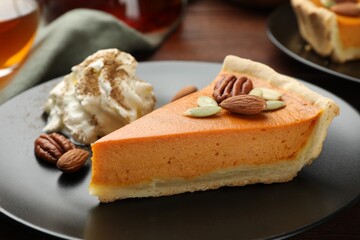 Piece of tasty homemade pumpkin pie with whipped cream, seeds and nuts on table, closeup