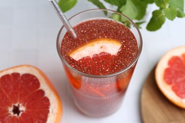 Glass of drink with chia seeds and grapefruit on white tiled table, closeup