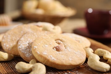 Tasty cashew cookies with powdered sugar on wooden board, closeup
