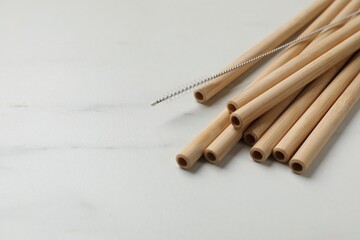 Bamboo drinking straws and cleaning brush on white marble table, closeup. Space for text