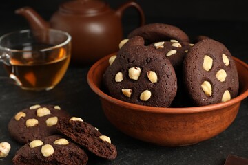 Tasty chocolate cookies with hazelnuts and tea on black table, closeup