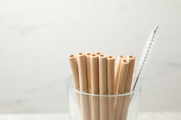 Bamboo drinking straws and cleaning brush in glass on blurred background, closeup