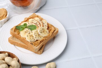 Tasty sandwich with peanut butter, apple, banana, chia seeds, nuts and mint on white tiled table, closeup. Space for text