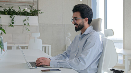 Professional Indian businessman Arabian muslim man happy male employer executive manager smiling working remote job in office workplace typing business project business online on laptop smile toothy
