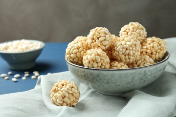 Tasty puffed rice balls in bowl on blue table, closeup