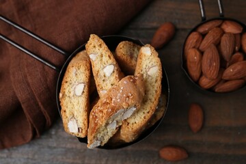 Tasty almond biscuits (Cantuccini) in scoop and nuts on wooden table, flat lay