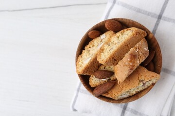 Tasty almond biscuits (Cantuccini) and nuts in bowl on white table, top view. Space for text