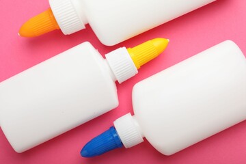 Bottles of glue on pink background, flat lay