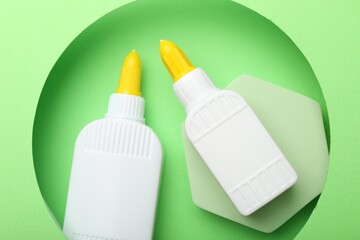 Bottles of glue on light green background, top view