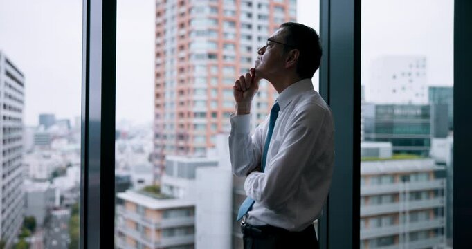 City, glass and thinking in office, businessman and ideas for case, lawyer and professional in law firm. Contemplating, window and planning for plea deal, legal and criminal defence attorney in Japan
