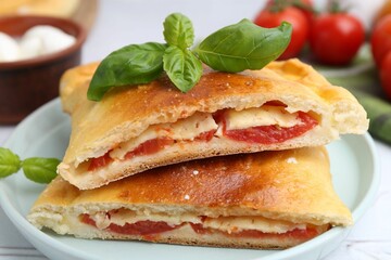 Pieces of tasty vegetarian calzone with tomato, cheese and basil on table, closeup