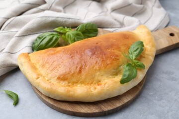 Tasty vegetarian calzone with basil on grey table, closeup