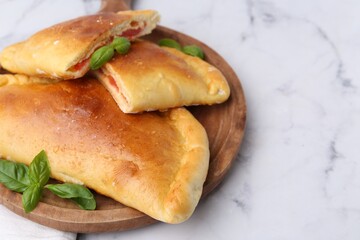 Tasty vegetarian calzones with tomato, cheese and basil on white marble table, closeup. Space for text