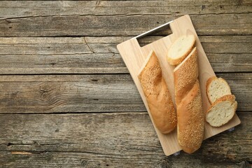 Cut fresh baguette with sesame on wooden table, top view. Space for text