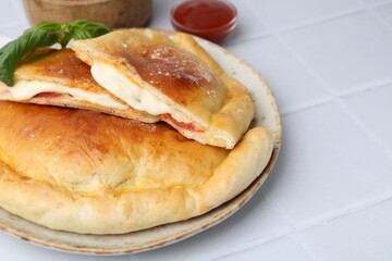 Pieces of delicious calzone pizza with mozzarella, tomatoes and basil on white tiled table, closeup