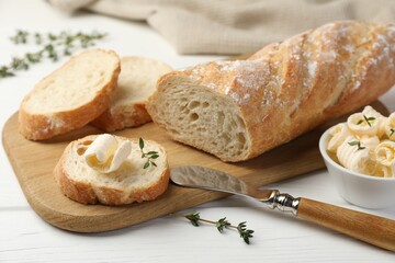 Cut baguette with butter and herbs on white wooden table, closeup