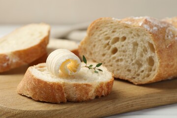 Cut baguette with butter and herbs on table, closeup