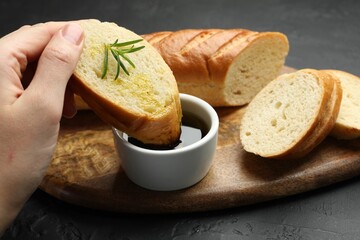 Woman dipping slice of tasty baguette into balsamic at black table, closeup