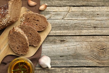 Slices of rye baguette, oil and garlic on wooden table, flat lay. Space for text