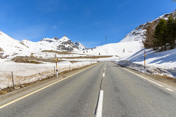 Naklejka premium Mountain pass road betweeen snowy slopes in the Swiss Alps under clear blue sky