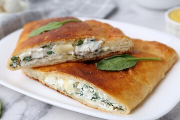 Pieces of tasty calzone with cheese and basil on white marble table, closeup