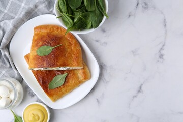 Pieces of tasty calzone with basil, mozzarella cheese and sauce on white marble table, flat lay. Space for text
