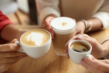 Women with cups of delicious coffee drinks at wooden table in cafe, closeup