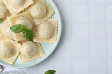 Delicious ravioli with cheese and basil served on white tiled table, top view. Space for text